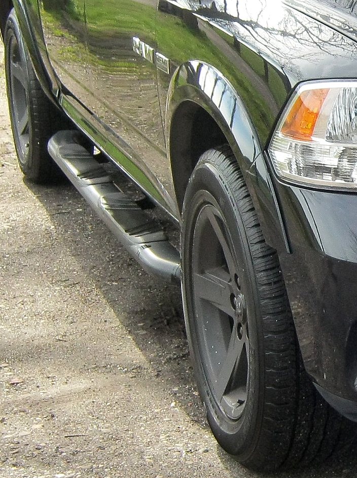 Zwarte velg met profielband en treeplank van een Dodge RAM 1500, vlak bij de voorwielkast